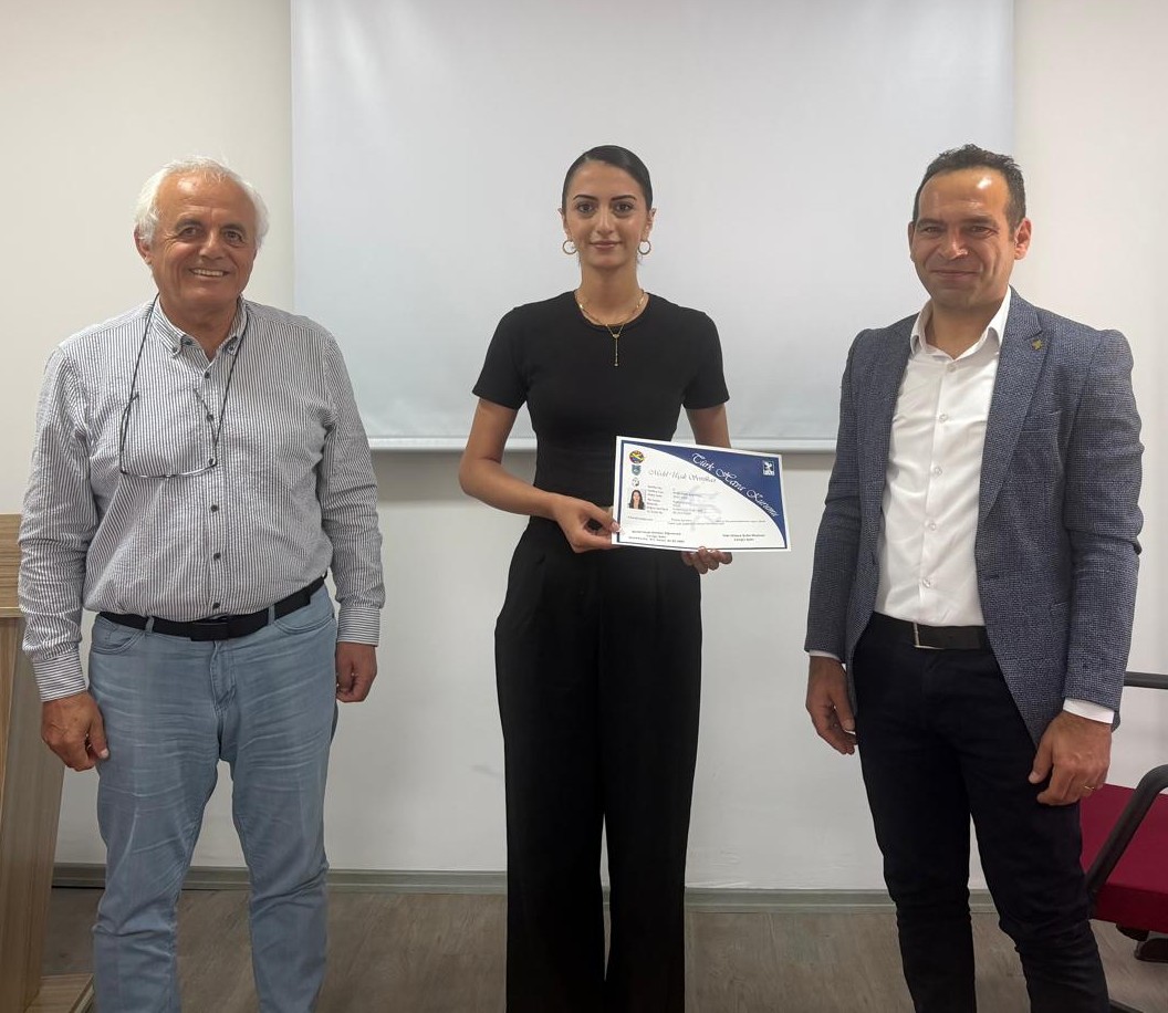 A female student dressed in elegant black attire poses with her certificate alongside Cengiz Şatır and Ozan Kaya.